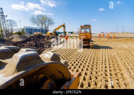 Blick über Walze mit Spikes auf Bulldozer, Bagger und LKW mit montierten Platte Vibrationsverdichter, wie sie verdichten, Nivellierung Sand für Straße Stockfoto