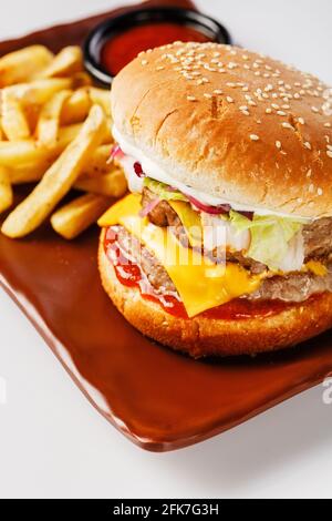 Burger. Saftiges Schweinekotelett, Cheddar-Käse, knusprig eingelegte Zwiebeln, in ein Brötchen gewickelter Salat unter zwei Saucen. Serviert mit pommes Frites und Sahnesauce. Stockfoto