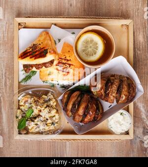 Street Food. Zitronentee, Salat, Bratkartoffeln mit Fleisch, Sauce und Rosmarin-Wurstbrötchen. Das Geschirr wird mit Einweggeschirr auf einem rustikalen Holz serviert Stockfoto