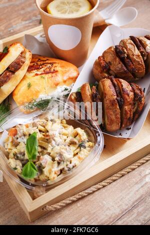 Einweggeschirr, Zitronentee, Schiefer, leckere Wurstbrötchen und Dill und gebackene Kartoffeln mit Fleisch auf einem Holztablett. Platz für Text. Straße fo Stockfoto