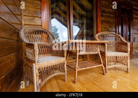 Schöne Außenterrasse mit Korbtisch und zwei Sesseln auf Holzbalkon. Stockfoto