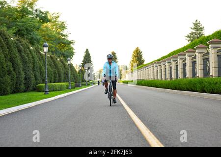 Ganzkörperaufnahme eines professionellen Rennradfahrers in Sportbekleidung Und Schutzhelmtraining im Park Stockfoto