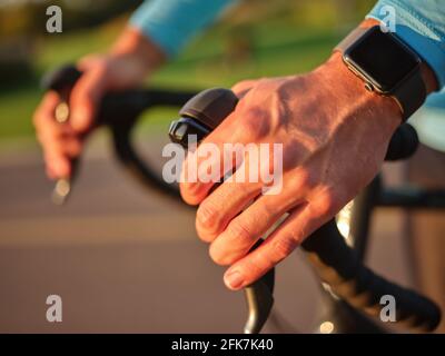 Nahaufnahme der Hände am Lenker. Radprofi mit Smartwatch beim Radfahren im Freien bei Sonnenuntergang Stockfoto