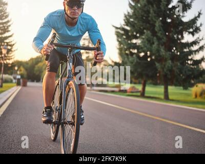 Radsportler mit Sportbekleidung, Schutzhelm und Brille, die während der Sommersaison auf der Parkstraße trainiert und konzentriert aussieht Stockfoto