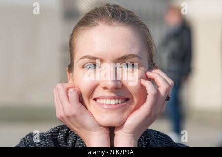 Portrait eines schönen jungen blonden Haares, das mit Gesicht in den Händen die Kamera anschaut und das Leben genießt, sonnenbaden, träumen und entspannen im Frühling Stockfoto