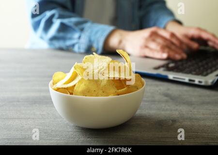 Schüssel mit Kartoffelchips gegen Frau, die am Laptop arbeitet Stockfoto