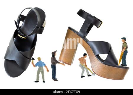 Mini-Männer arbeiten an schwarzen High-Heel-Schuhen mit offenem Zehenbereich und überkreuztem Riemen, Plattform-Sandalen mit braunem Blockabsatz, Knöchelriemen wird mit Metallbuck befestigt Stockfoto