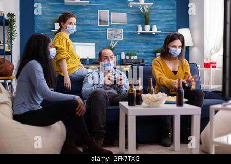 Fröhliche Gruppe von multiethnischen Freunden feiern den Sieg spielen Videospiele Wettbewerb mit Wireless-Controller im Wohnzimmer sitzen auf der Couch. Popcorn- und Bierflaschen. Stockfoto
