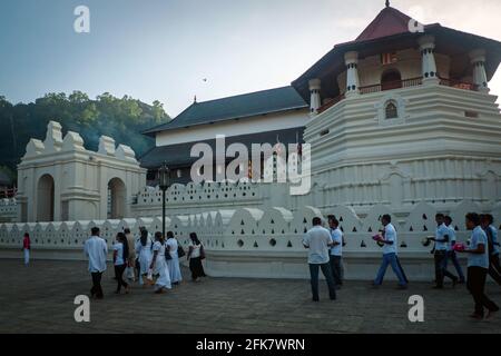 Kandy, Sri Lanka: Einige weiß gekleidete Menschen gehen im Morgengrauen in den Tempel der heiligen Zahnreliquie (Sri Dalada Maligawa) Stockfoto