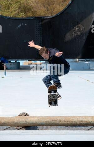 Mit der Unisphere Base im Hintergrund springt ein Skateboarder über eine Hürde. Im Flushing Meadows Corona Park in Queens, New York City Stockfoto