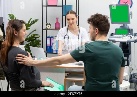 Ein Ehepaar sitzt in einem Büro mit einem Gynäkologen. Der Mann unterstützt seine Schwangeren. Grüner Bildschirm Stockfoto