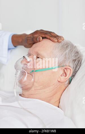 Nahaufnahme eines afroamerikanischen Arztes, der ältere Patienten tröstet und darin liegt Krankenhausbett mit Sauerstoffmaske Stockfoto