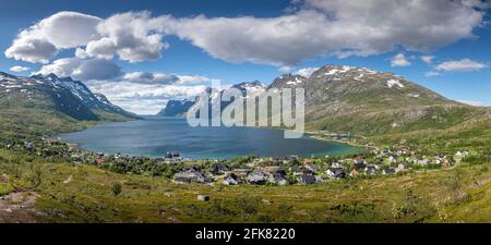 Sommer Fjordpanorama mit Dorf am Ende des Fjords. Berge bedeckt mit Schnee und schönen Wolken über dem Meer Stockfoto