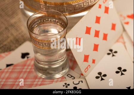 Spielkarten, ein Glas Wodka und ein Dekanter Wodka auf einem Tisch, der mit grobem Sackleinen bedeckt ist. Nahaufnahme, selektiver Fokus. Stockfoto