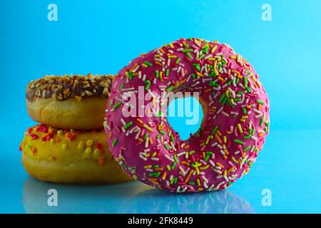 Ein Stillleben Food Donut berliner in einer rosa Glasur mit einem farbigen Ständer von Donuts auf einem blauen hellen Hintergrund . Stockfoto