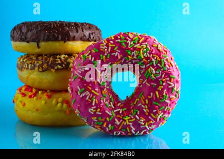 Ein Stillleben Food Donut berliner in einer rosa Glasur mit einem farbigen Ständer von Donuts auf einem blauen hellen Hintergrund . Stockfoto