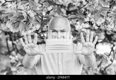 Gesichtsmaske des älteren Mannes. Atemmaske. Pollenallergen. Mann und Blumen. Allergische Reaktion. Begrenzen Sie die Ausbreitung von Infektionen. Atembeschwerden Stockfoto