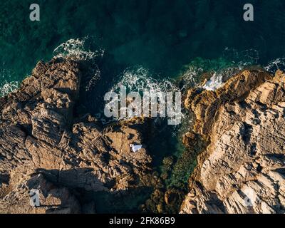 Braut und Bräutigam stehen mit Händen auf den Felsen am Meer und schauen sich gegenseitig an, Draufsicht Stockfoto