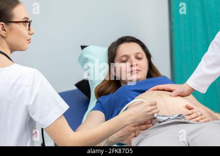 Eine Krankenschwester untersucht den Bauch mit einem Ultraschallgerät, und ein Arzt berührt den Bauch eines Schwangeren sanft. Stockfoto