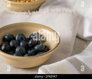 Frische Blaubeeren in einer rustikalen Steingut-Schale auf beigem Tisch Hintergrund Stockfoto