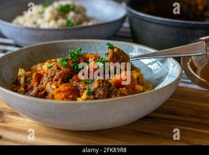 Köstlicher Rindereintopf mit braunem Reis, Sauce und Karotten auf einem rustikalen Teller auf Holztischhintergrund. Nahaufnahme Stockfoto