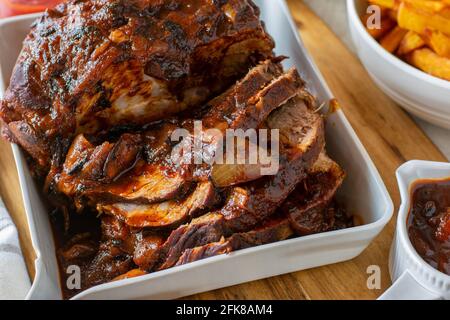Schweinebraten mit Barbecue-Sauce serviert mit frischen hausgemachten französisch Pommes auf einem Küchentisch Stockfoto