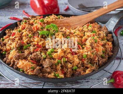 Mediterrane Pfanne mit serbischem Djuvec-Reis und würzigem Hackfleisch, serviert in einer rustikalen gusseisernen Pfanne auf verwittertem Holzhintergrund. Stockfoto