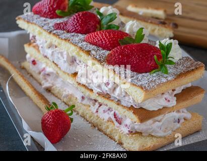 Hausgemachte Erdbeer-Sahnetorte mit frisch gebackenem Biskuitteig Und serviert mit frischen Erdbeeren auf einem rustikalen Küchentisch Hintergrund Stockfoto