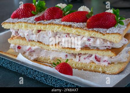Hausgemachte Erdbeer-Sahnetorte mit frisch gebackenem Biskuitteig Und serviert mit frischen Erdbeeren auf einem rustikalen Küchentisch Hintergrund Stockfoto