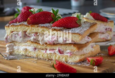 Hausgemachte Erdbeer-Sahnetorte mit frisch gebackenem Biskuitteig Und serviert mit frischen Erdbeeren auf einem rustikalen Küchentisch Hintergrund Stockfoto