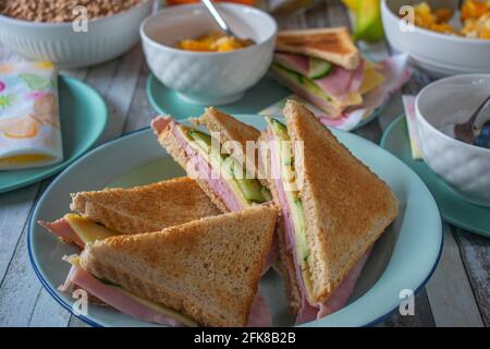 Ein Teller mit getoasteten Sandwiches auf einem Frühstückstisch mit Obst und Müsli zu Hause. Stillleben Stockfoto