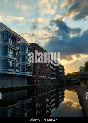 Eine dramatische Sturmwolke verdunkelte den Sonnenuntergang hinter einigen Wohnungen, die Teil eines Regenerationsprojekt waren und sich alle in stillem, glasigen Kanalwasser widerspiegelten. Stockfoto