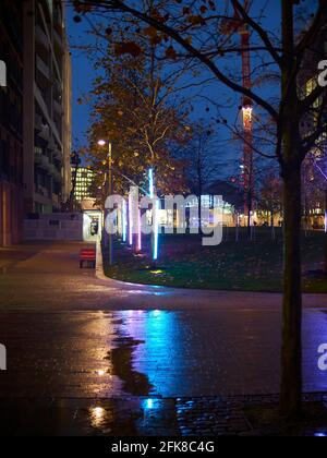 Ein Pfad und ein Park, Teil eines Verjüngungsprojekts, bei Winterregen, der den Boden nass gemacht hat und scharfe Neonreflexe zum Schimmern gebracht hat. Stockfoto