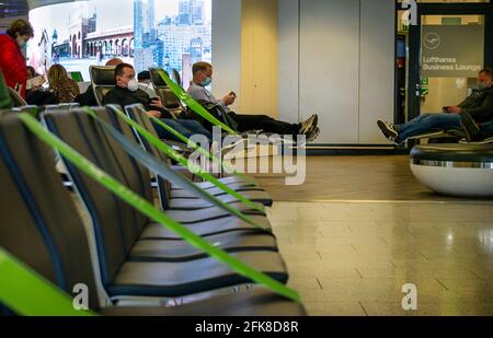 Eine Reihe von schwarzen leeren Sitzen. Passagiere in der Transitzone des Frankfurter Flughafens, die im Sitzbereich mit einer Entfernung, die durch grünes Klebeband gekennzeichnet ist, warten. Stockfoto