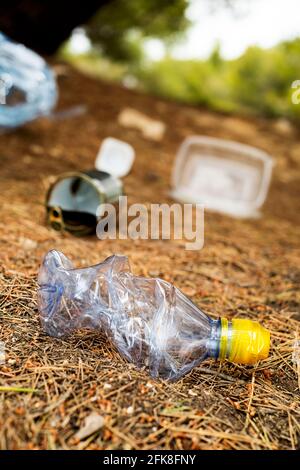 Nahaufnahme einer gebrauchten Plastikflasche und einiger anderer Abfälle, wie gebrauchte Lebensmitteldosen und Plastikbehälter, die auf den Boden eines Waldes geworfen werden Stockfoto