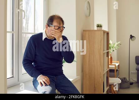 Verzweifelter reifer Mann, der allein auf einer Fensterbank sitzt und weint Über das Leben Probleme Stockfoto