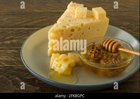 Radamer Käse auf einem Teller serviert mit Honig. Dreieckiges Stück gelbe Kuhmilch schweizer Käse mit Löchern. Stockfoto