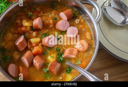 Draufsicht auf einen Topf mit frisch gekochtem Karotteneintopf mit Kartoffeln, Wurzelgemüse und gekochten Würstchen Stockfoto