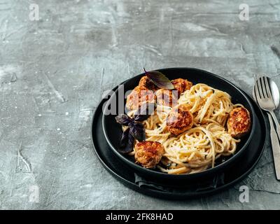 Zucchini Parmesan Fleischbällchen mit Pasta Carbonara in schwarzem Craft Teller auf grauem Hintergrund. Nahaufnahme von cremigem Carbonara mit Kopierraum links Stockfoto