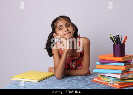 Kleine indische Mädchen denken oder träumen während der Vorbereitung Hausaufgaben. Mit Stapel von Büchern Stockfoto