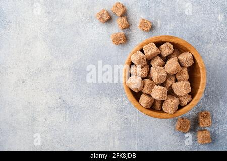 Rohrzucker-Würfel in Bambusschüssel auf grauem Tischbetonhintergrund. Draufsicht. Stockfoto