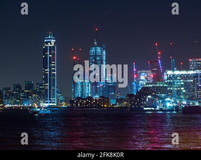 Ein dunkler Nachthimmel durchbohrt mit hellen künstlichen Lichtern von Wolkenkratzern und Kränen einer Londoner Stadtlandschaft, die sich im gewellten Flusswasser spiegeln. Stockfoto