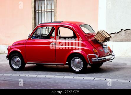 Stilvolle kleine rote italienische Oldtimer. Seitenansicht. Alte Grunge Haus Stuckfassade im Hintergrund. Gewebt Holzlager und Gepäckkasten auf der hinteren Haube Stockfoto