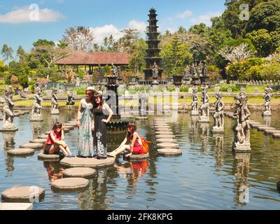 Eine Gruppe von Touristen posiert in dem erstaunlichen Teich, der voller exotischer Steinskulpturen und einem hohen Brunnen ist. Im Tirta Gangga Water Palace in Bali, Ind Stockfoto