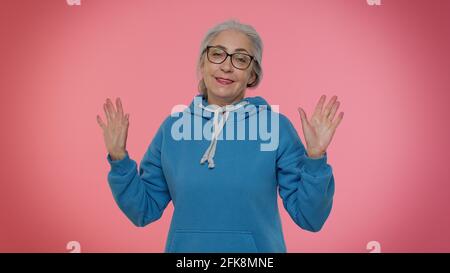 Eine fröhliche, freundliche ältere Frau winkt mit der Handfläche in einer Hello-Geste Begrüßt positive Emotionen von jemandem Stockfoto