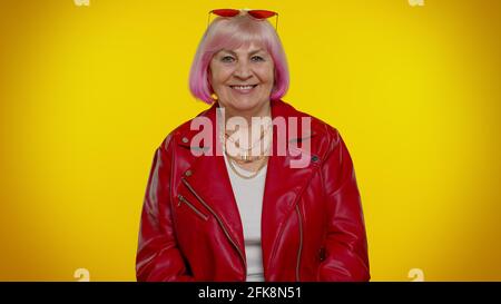 Fröhliche stilvolle Senior Oma Frau mit rosa Haaren in roter Lederjacke lächelnd, Blick auf die Kamera Stockfoto