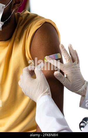 Beschnittene Ansicht des Arztes in Latexhandschuhen, die Klebstoff-Gips auftragen Am Arm des afroamerikanischen Patienten isoliert auf weiß Stockfoto