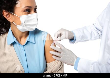 afroamerikanischer Patient in medizinischer Maske sitzt in der Nähe des Arztes applying Klebestreifen isoliert auf weiß Stockfoto