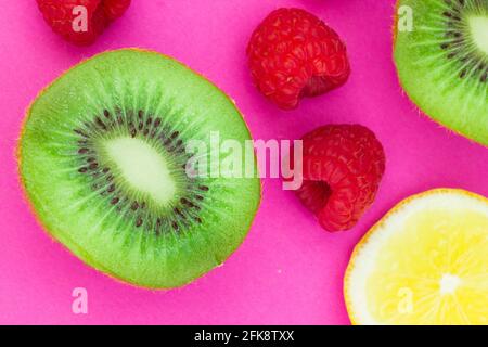 Halbiert geschnittene Kiwi-Früchte, Himbeeren und Zitrone auf rosa Hintergrund Stockfoto