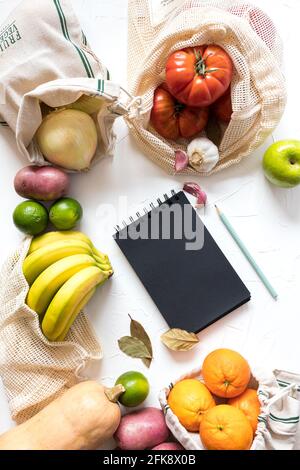Buntes Gemüse in ökologischen Taschen um einen Einkaufslistenblock. Stockfoto